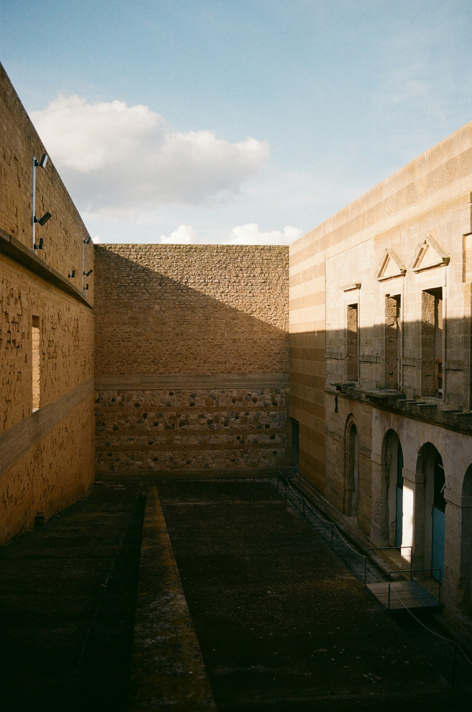 A limestone courtyard with whitewashed walls, arched openings, and strong afternoon shadows.