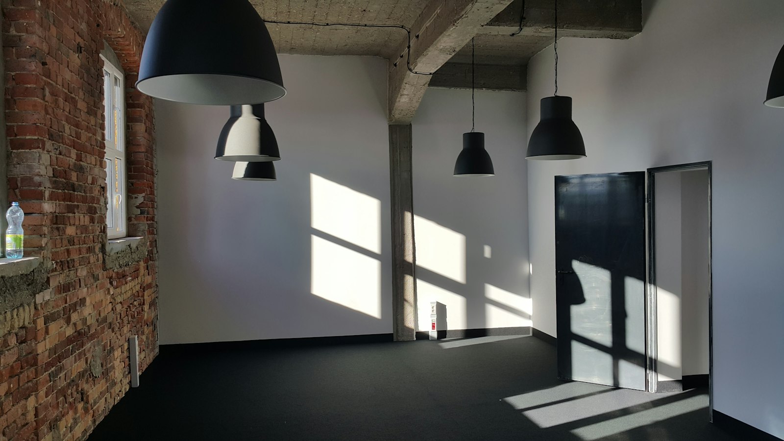 Sunlight streams through a tall window into a brick industrial hall with a sawtooth roof.